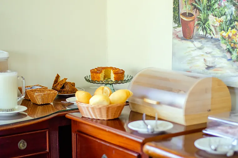 Bolo caseiro na boleira e cesta de pão francês no café da manhã da Petit Refuge