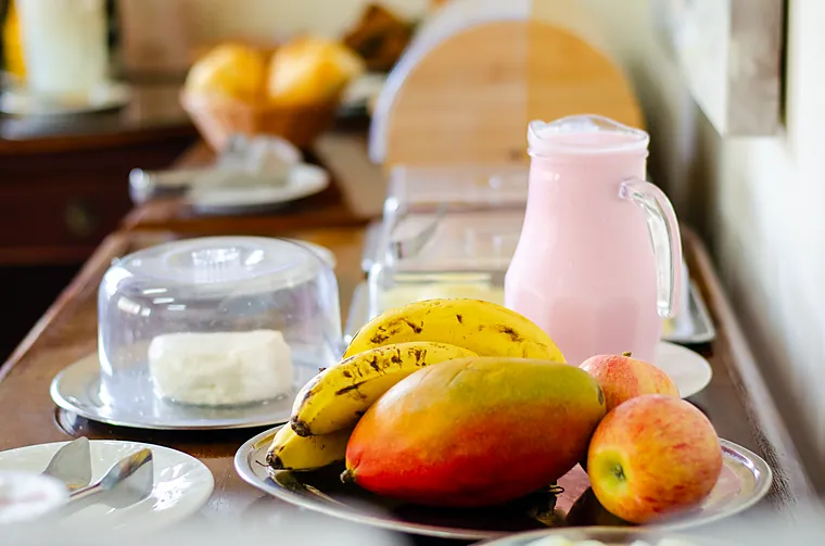 Bandeja com banana, manga e maçã ao lado da jarra de vitamina no café da Petit Refuge