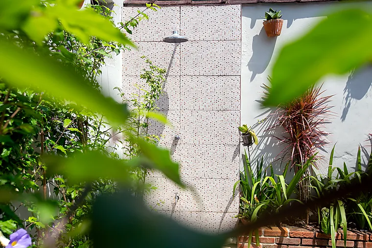 Ducha externa de pastilha branca cercada de plantas na Pousada Petit Refuge
