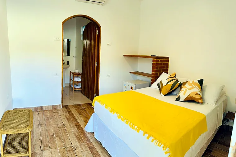 Junior com vista para o jardim da Pousada Petit Refuge com cama de casal, frigobar e arco de alvenaria para o banheiro