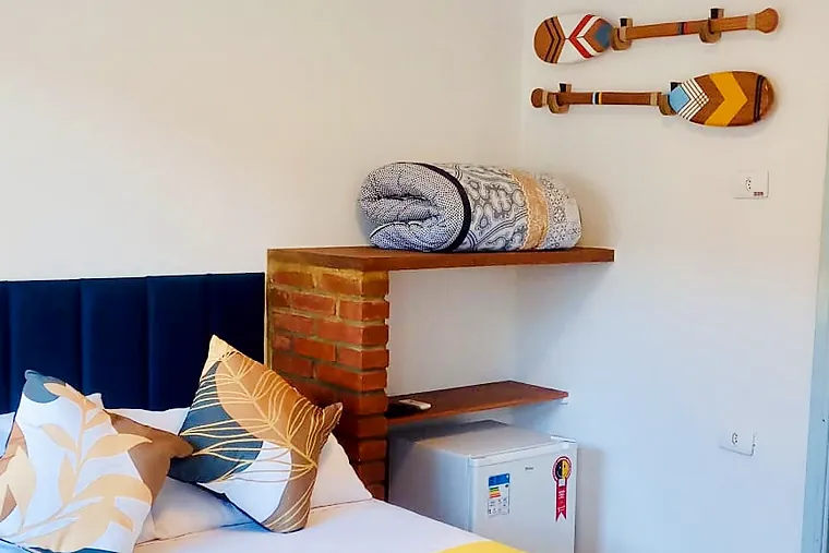 Cama de casal do Junior com vista para o jardim da Petit Refuge ao lado do nicho de tijolo com prateleiras